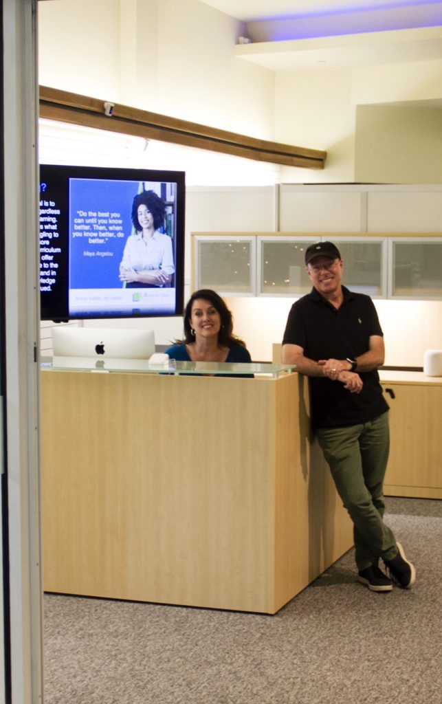 Two people standing at a reception desk in front of a television.