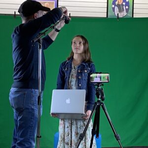 A man taking a picture of a woman in front of a green screen.