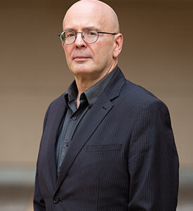 A bald man in glasses and a black jacket.