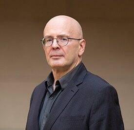 A bald man in glasses and a black jacket.