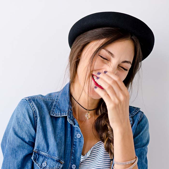 A woman in a hat is laughing and holding her face.