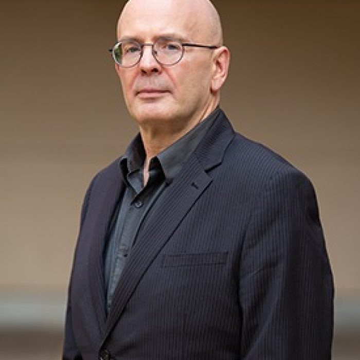 A bald man in glasses and a black jacket.
